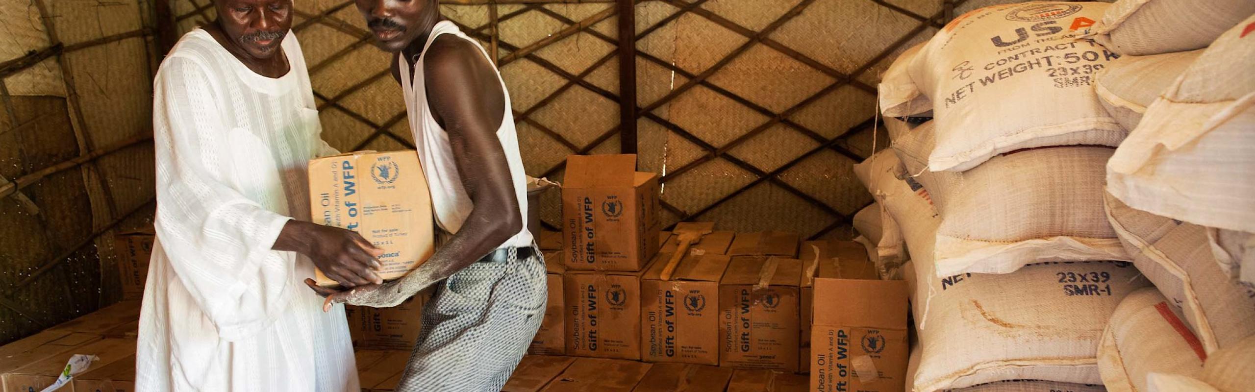 Two men in Darfur carry boxes of food aid, including wheat. Supply disruptions and rising prices of wheat and other items are causing problems for countries in the Middle East and elsewhere as the Russia-Ukraine war continues.