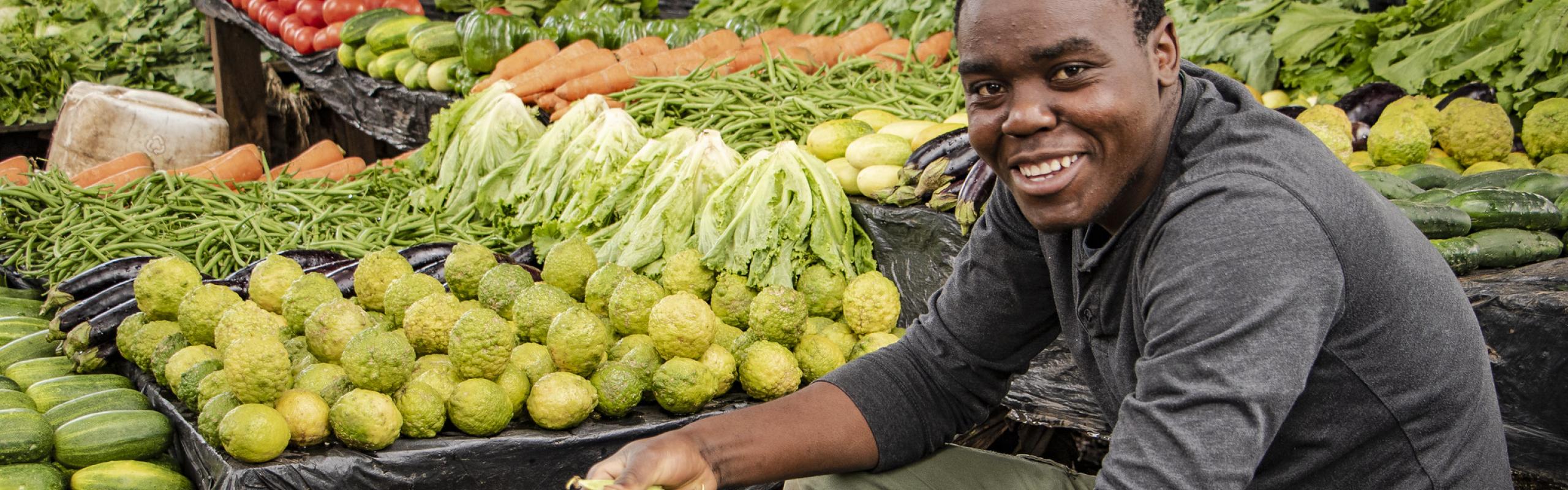 Man sits shelling peas among produce stands at Lizulu Market in Malawi's capital, Lilongwe