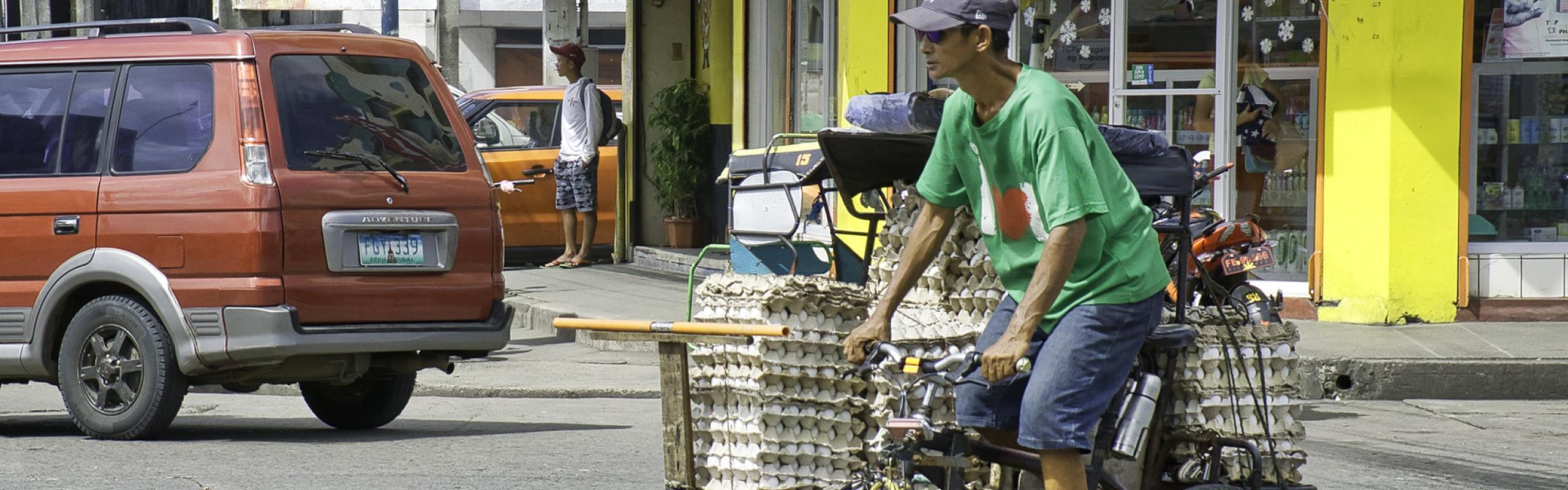 Man rides bicycle delivering trays of eggs to local market in Bacolod City, Philippines