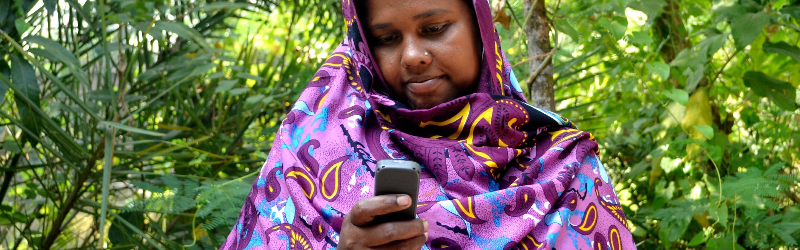 Female farmer in Bangladesh, dressed in purple headscarf, receives mobile money on her cellular phone