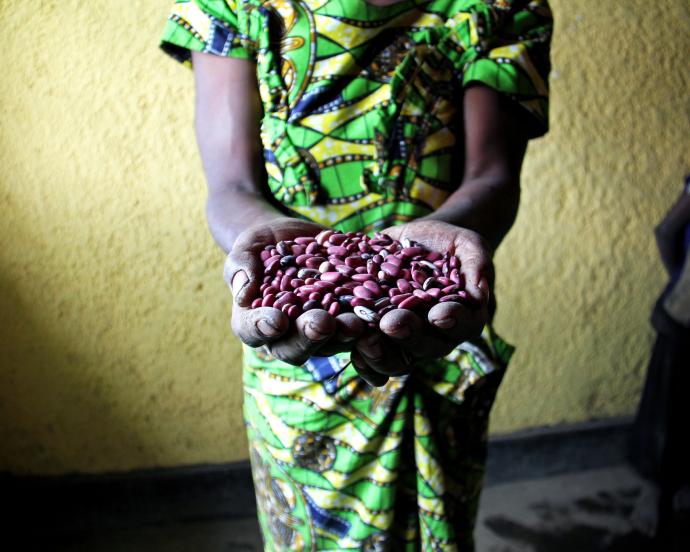 Person in green and yellow wrap holds out handful of dried red beans