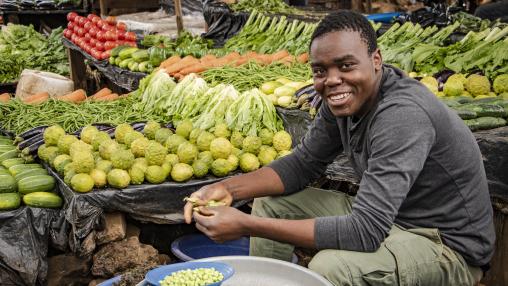Man sits shelling peas among produce stands at Lizulu Market in Malawi's capital, Lilongwe