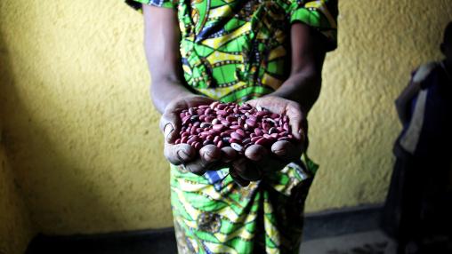 Person in green and yellow wrap holds out handful of dried red beans
